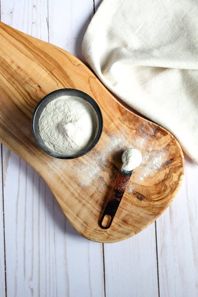 potato flour in a spoon sitting on a wooden cutting board.