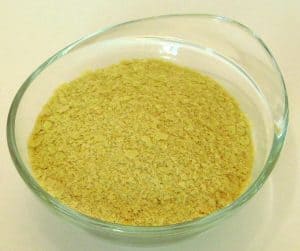 Clear bowl of dairy free nutritioanl yeast, sometimes used to make plant based cheese.