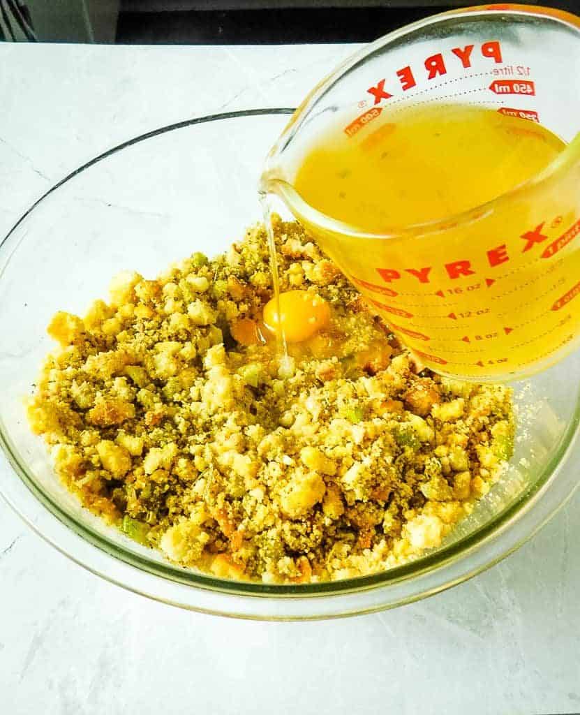 pouring broth into cornbread mix in a clear bowl