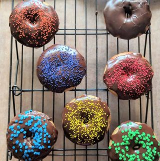 gluten free cake donuts baked with chocolate glaze sitting on a rack.