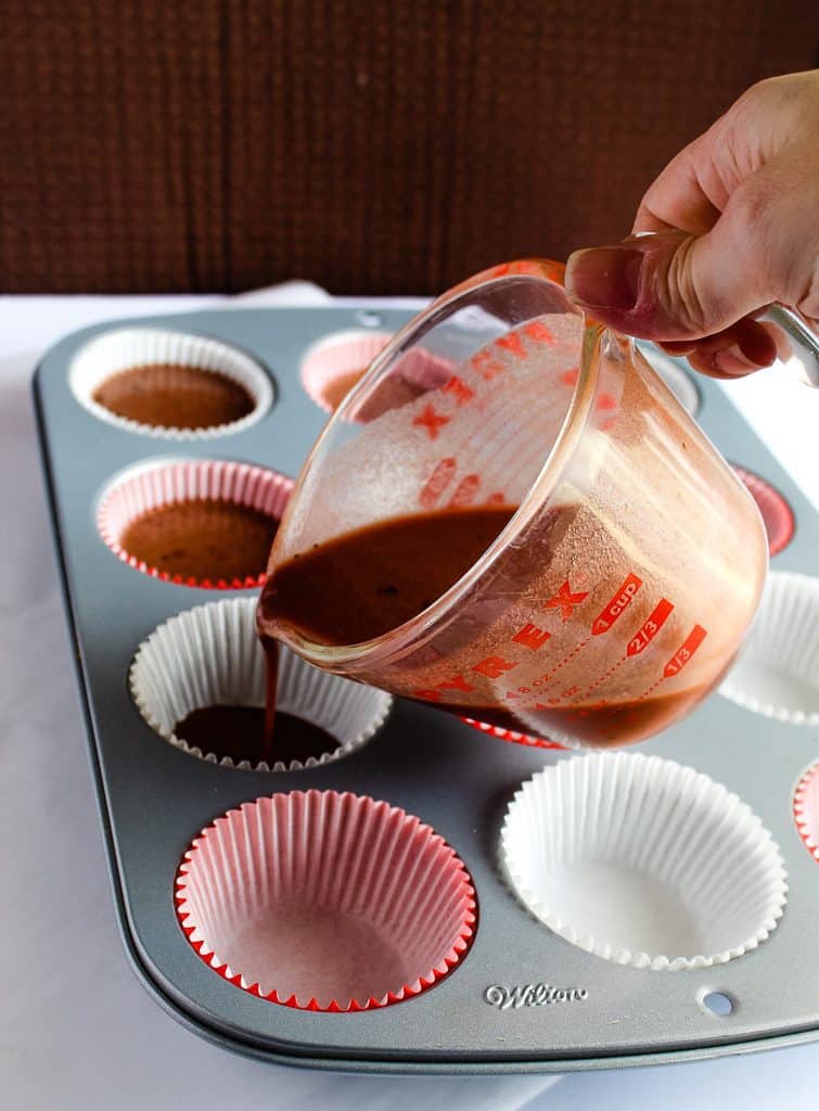 glass measuring cup pouring gluten free red velvet cupcake batter into cupcake liners