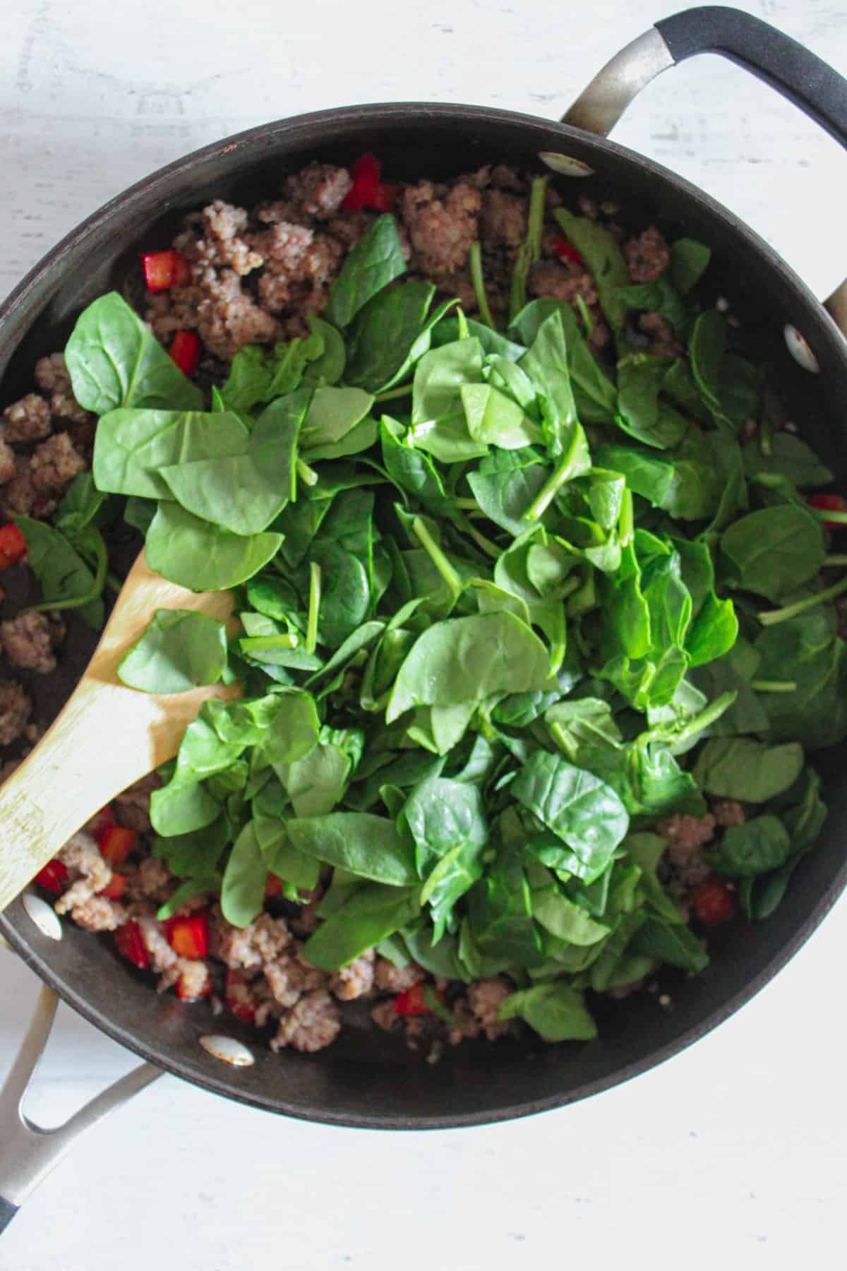 adding a bunch of spinach to the skillet.