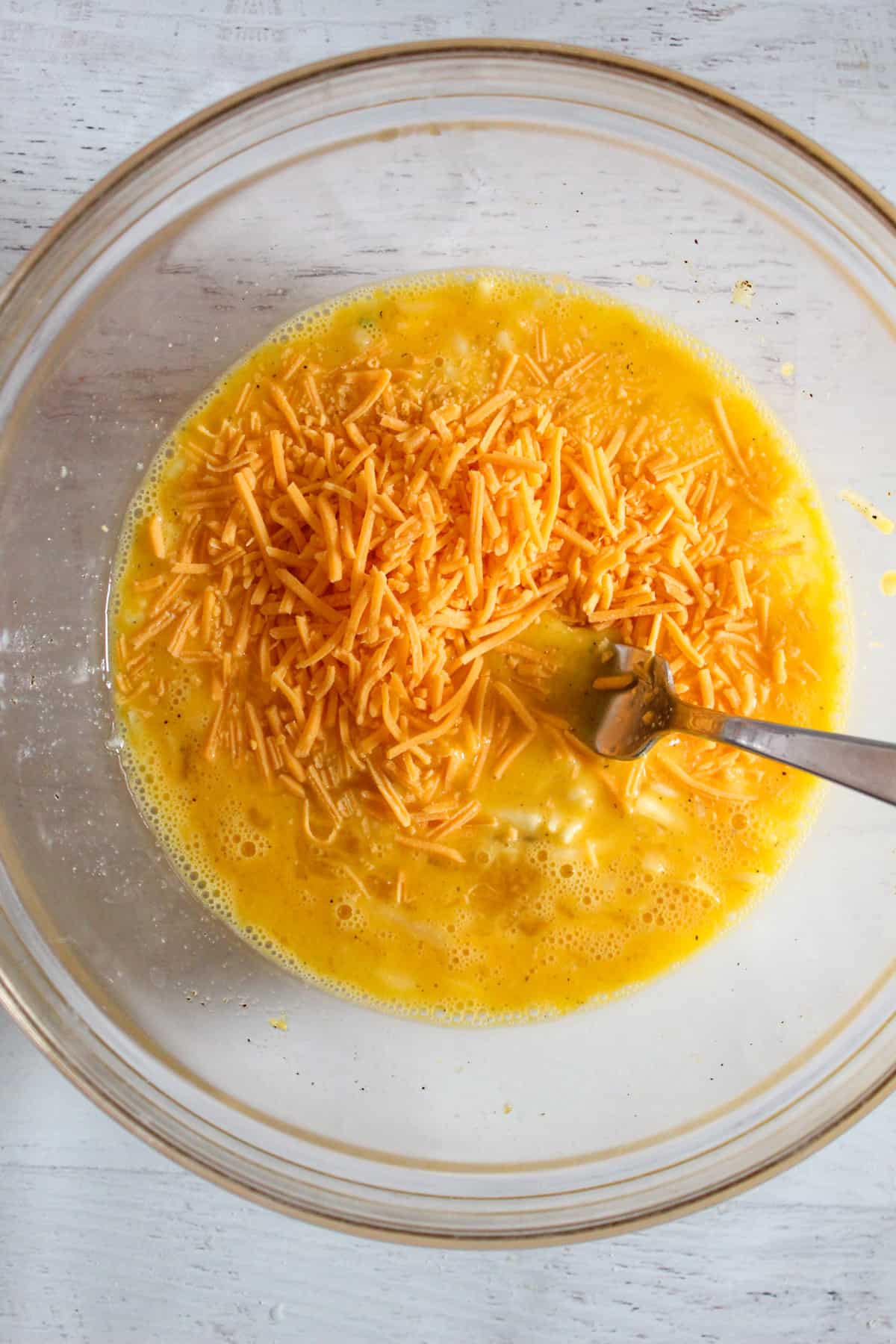 adding shredded cheese to a glass bowl of eggs.