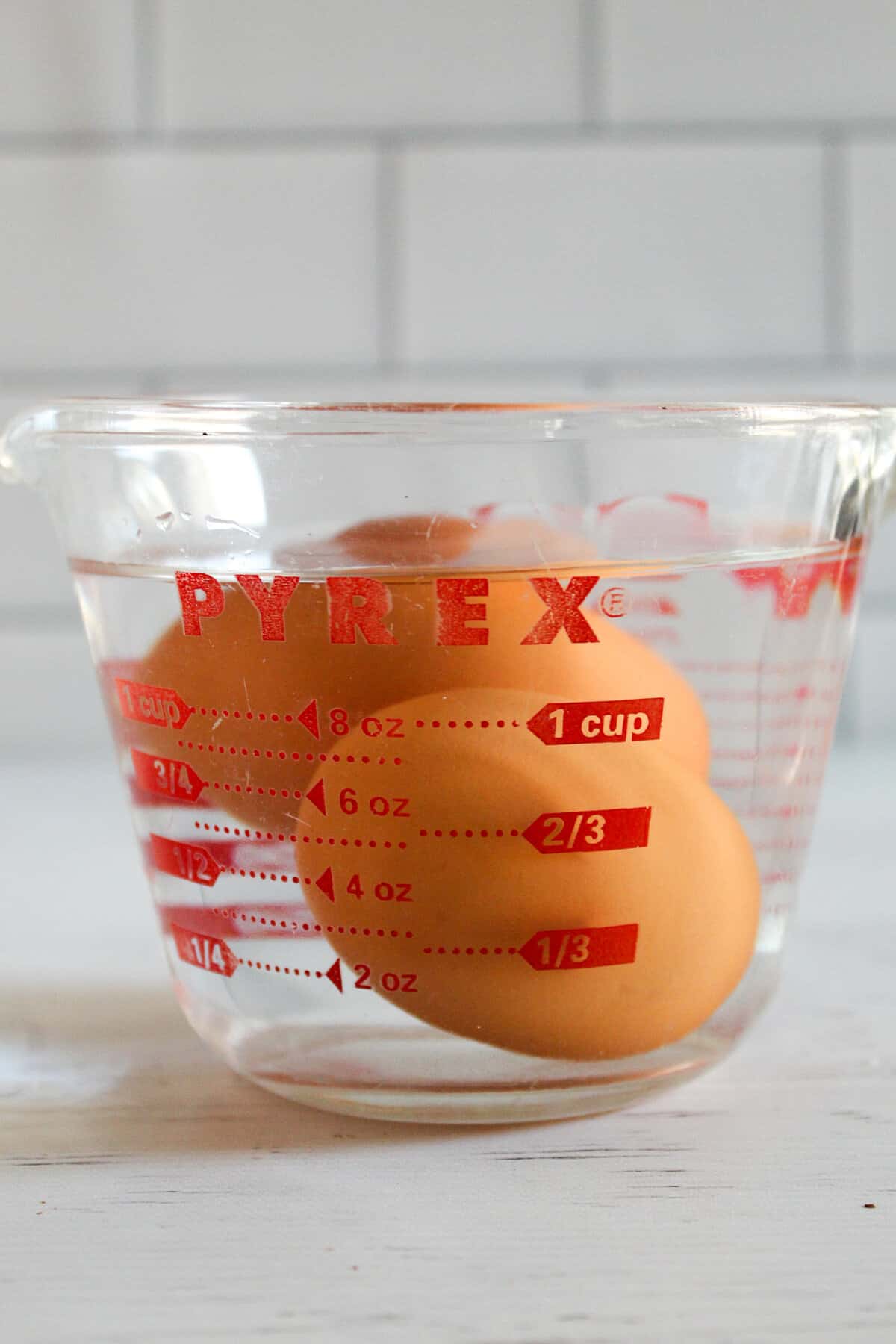 2 brown eggs floating in a glass of water.