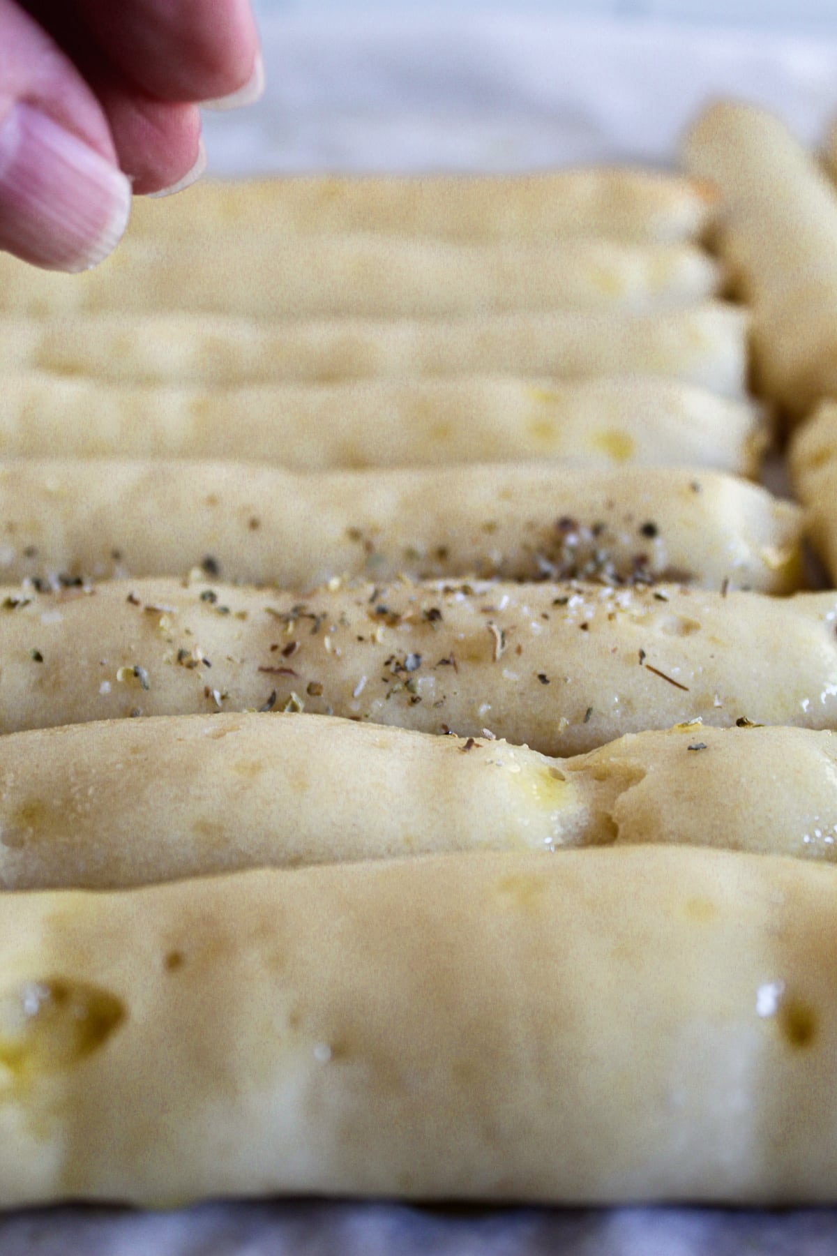 sprinkling baked bread sticks with italian seasoning.