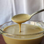 glass bowl of tahini running off a spoon