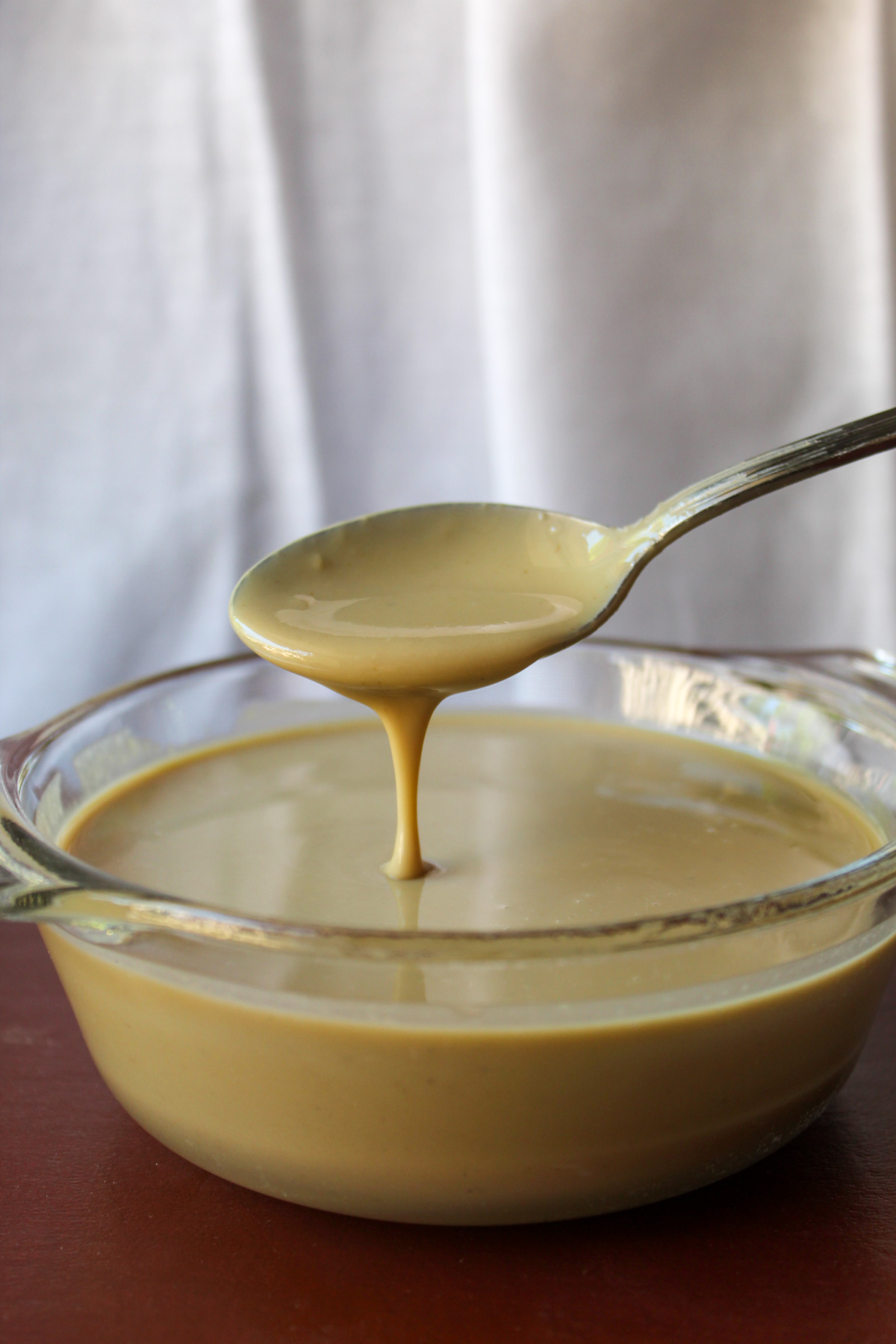 glass bowl of tahini running off a spoon