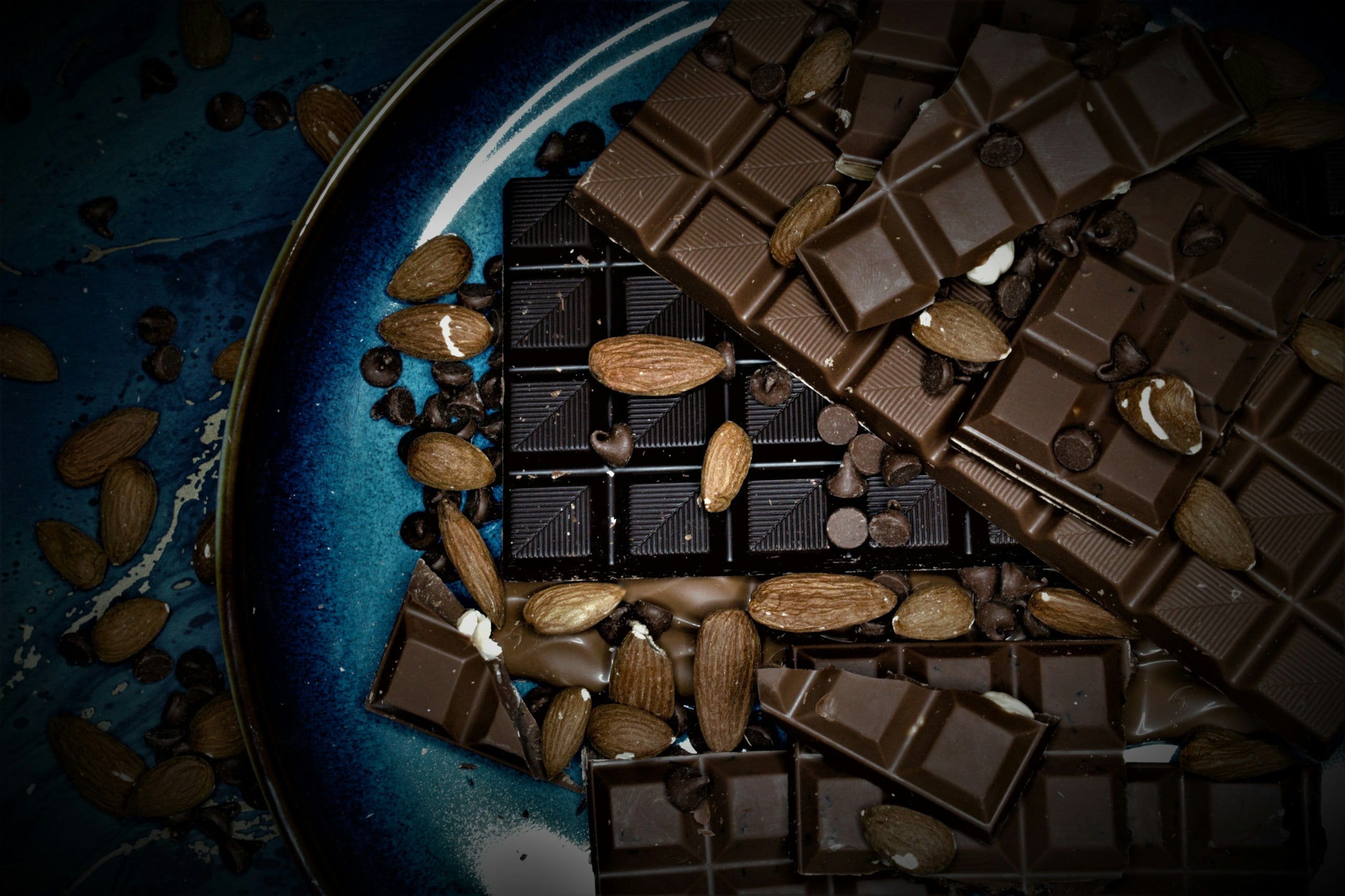 Unsweetened vs bittersweet Chocolate bar topped with almonds on a blue plate. 