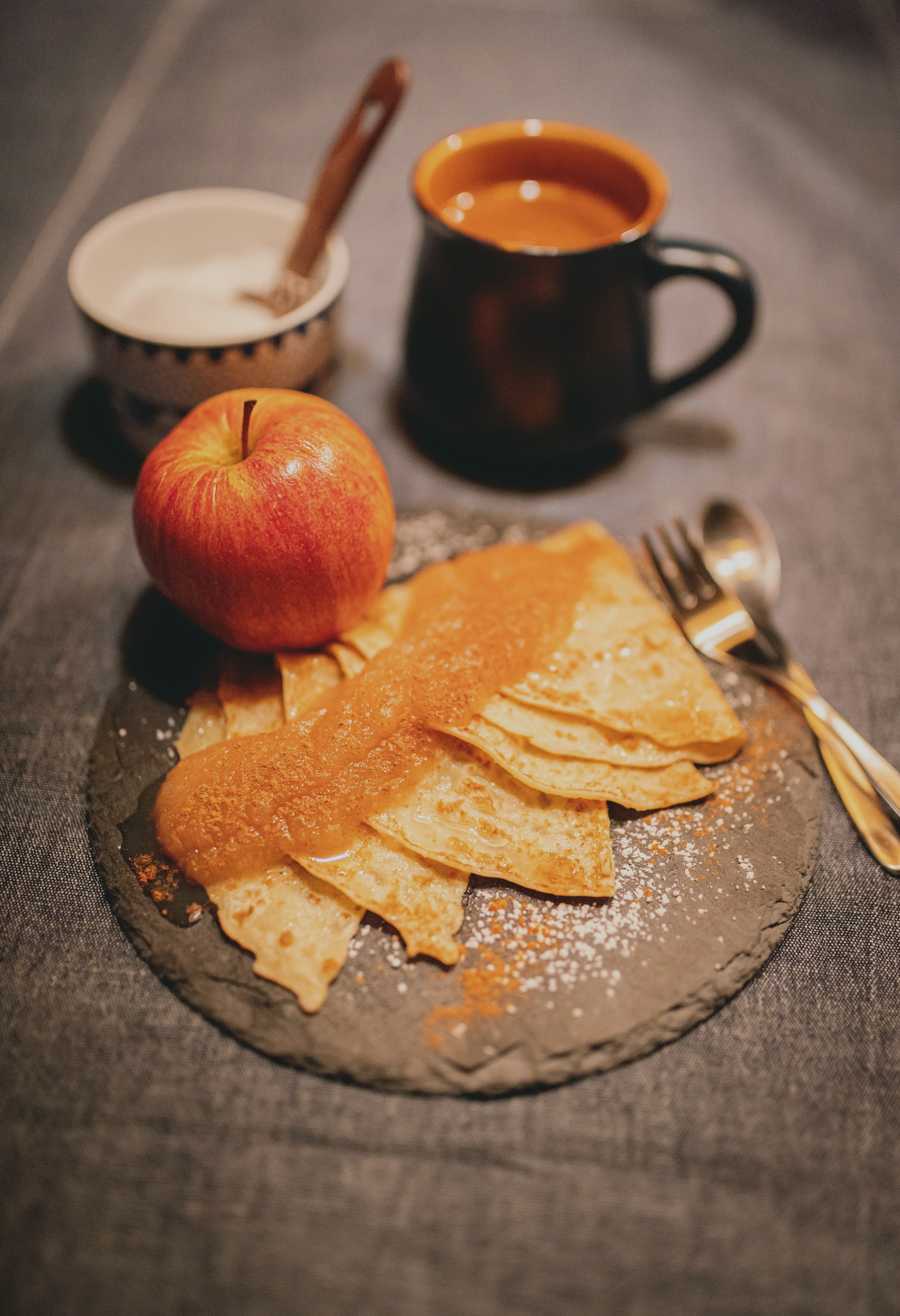 Red apple placed beside folded crepes topped with applesauce.