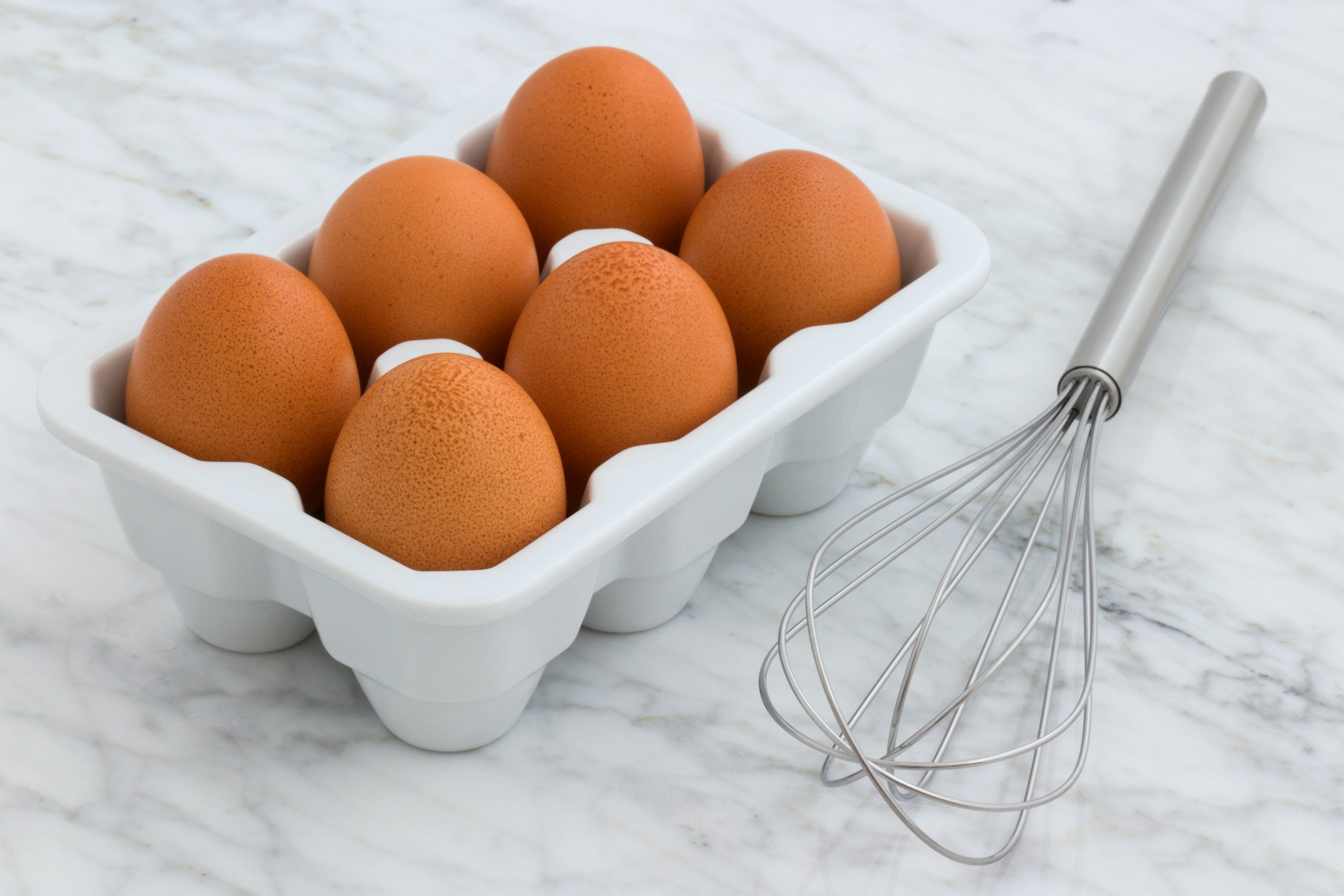 Six eggs in an egg container with whisk