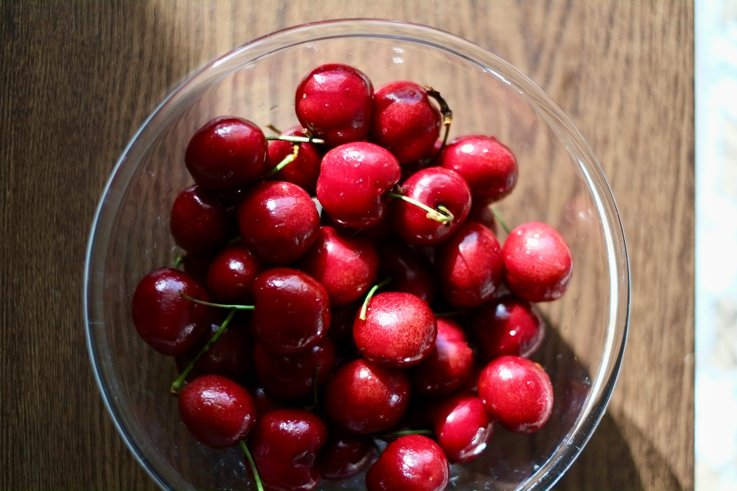 a glass bowl filled with cherries on top of a wooden table