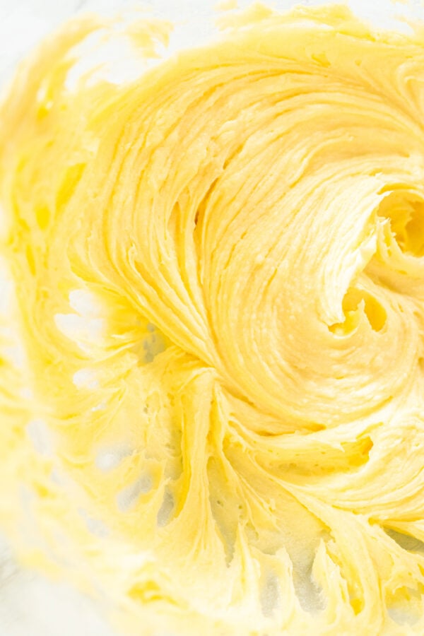 A smooth and fluffy mixture of butter and sugar is perfectly creamed in a glass mixing bowl, forming the base for lemon spritz cookie dough. The light, whipped texture ensures a soft, melt-in-your