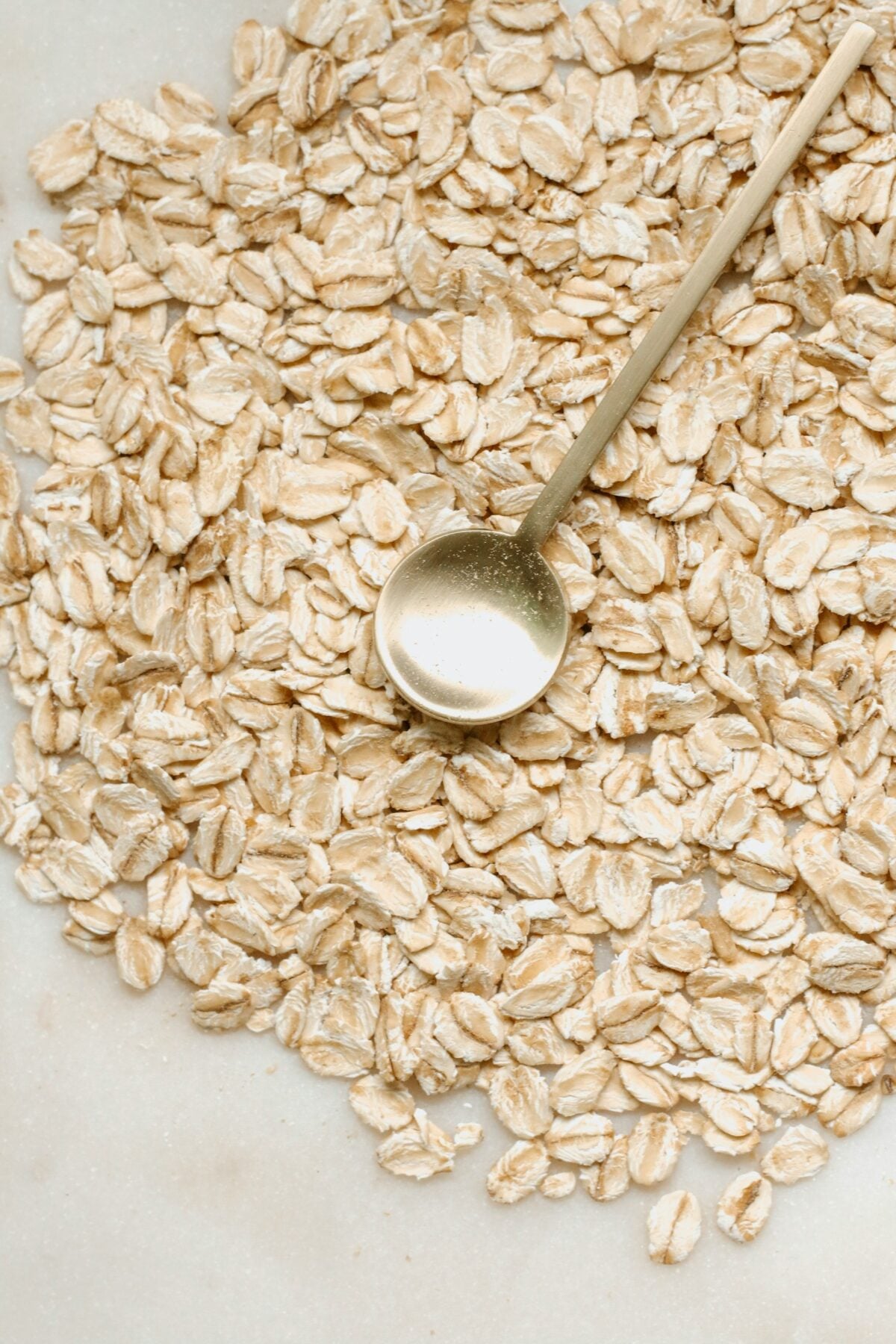 Golden spoon with oats on marble table.
