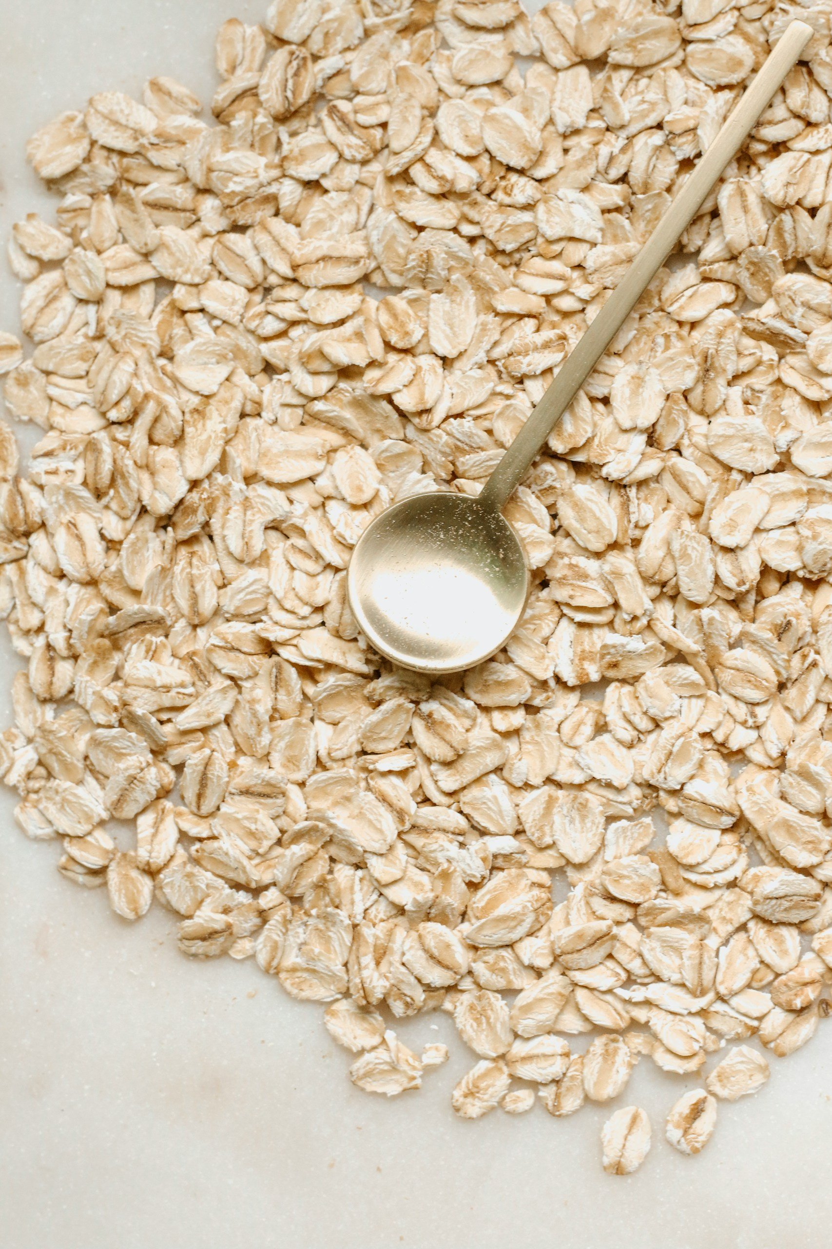 Golden spoon with oats on marble table.