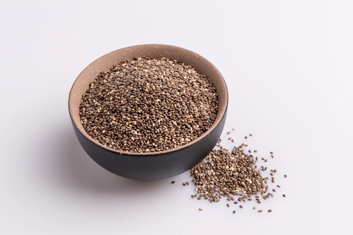 Grounded chia seeds (Salvia hispanica) in a brown ceramic bowl, isolated on white background